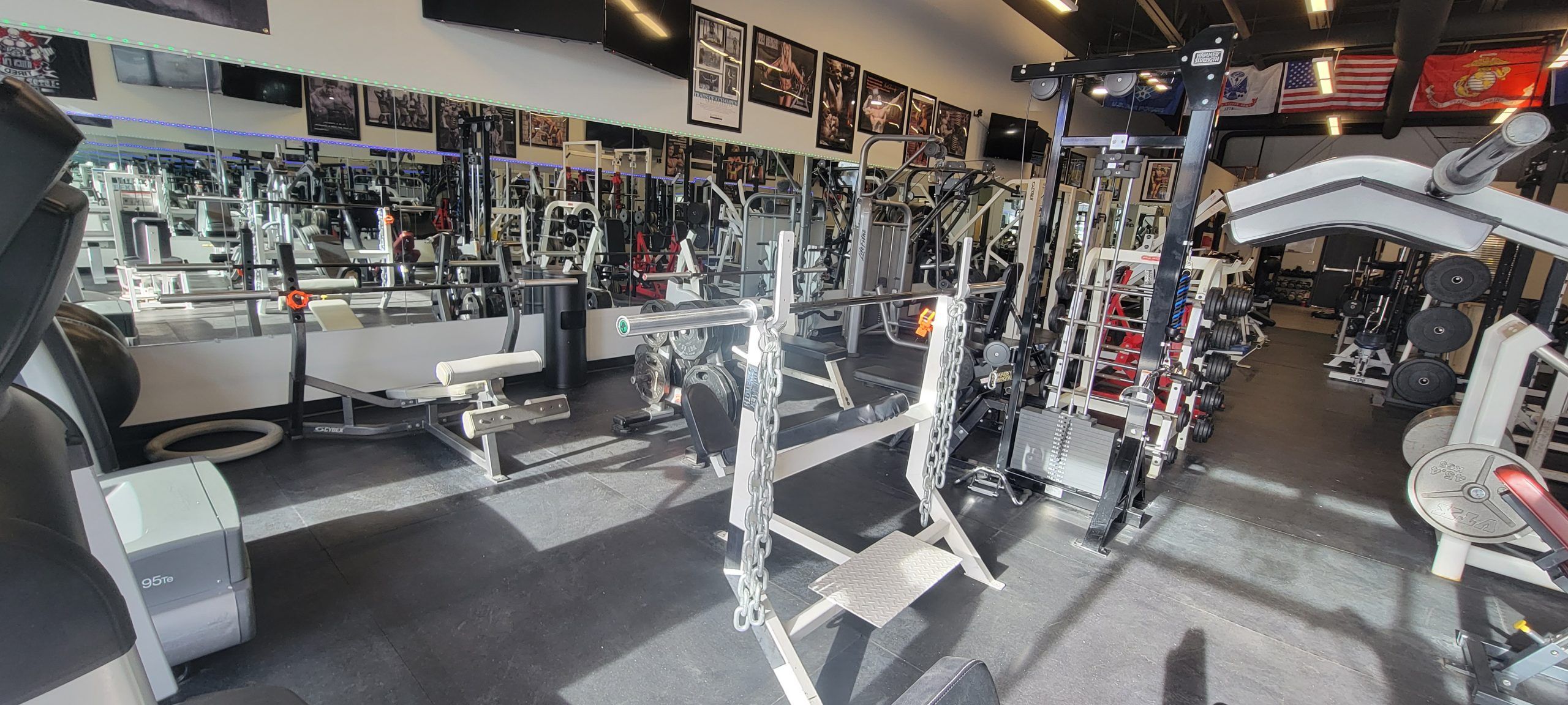 Bench station with chains hanging from the bar, beside squat racks and a mirrored wall