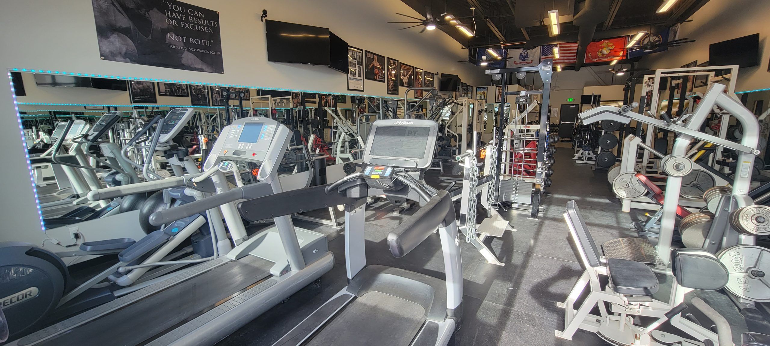Treadmills and elliptical trainers facing a mirrored wall, with plate-loaded machines behind them