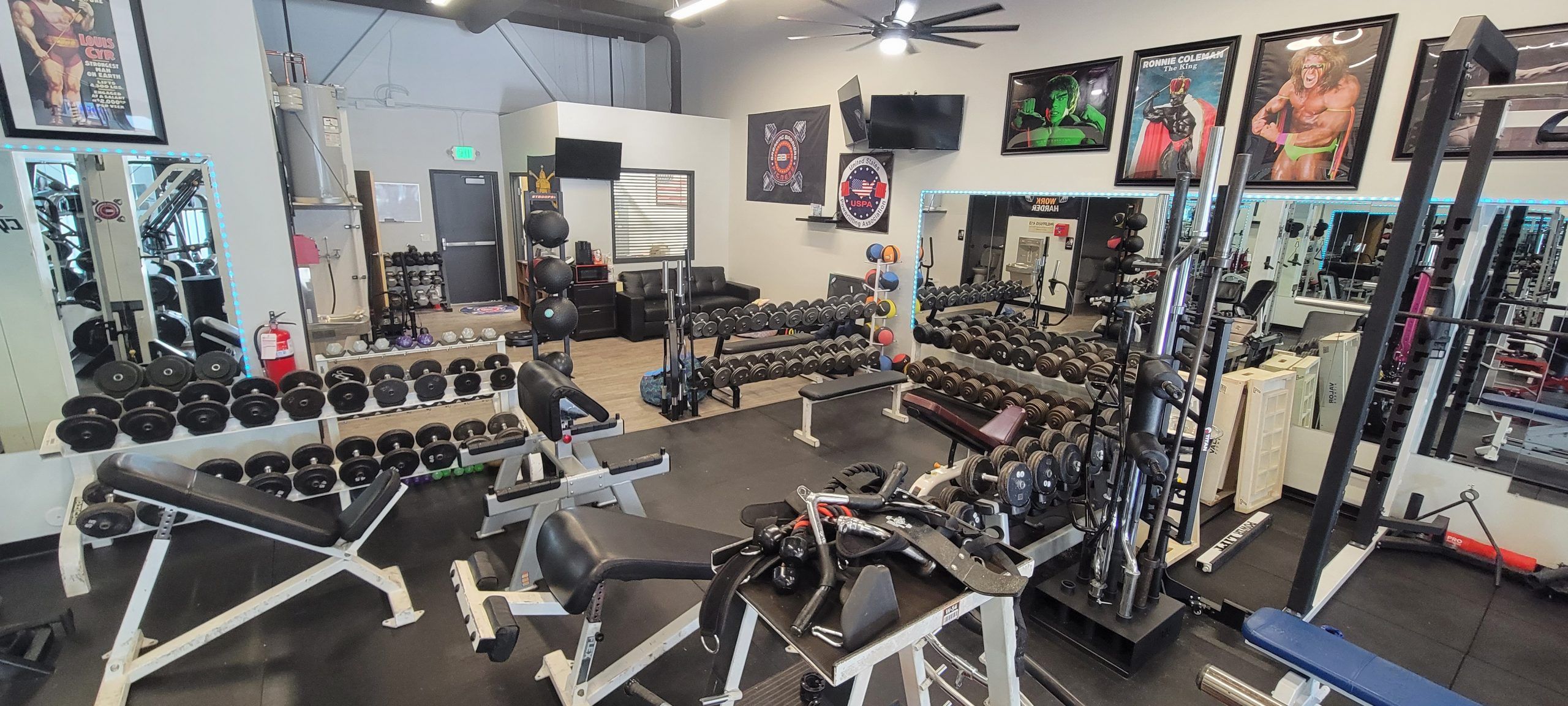Free-weight area with adjustable benches, dumbbell racks and bodybuilding posters on the wall