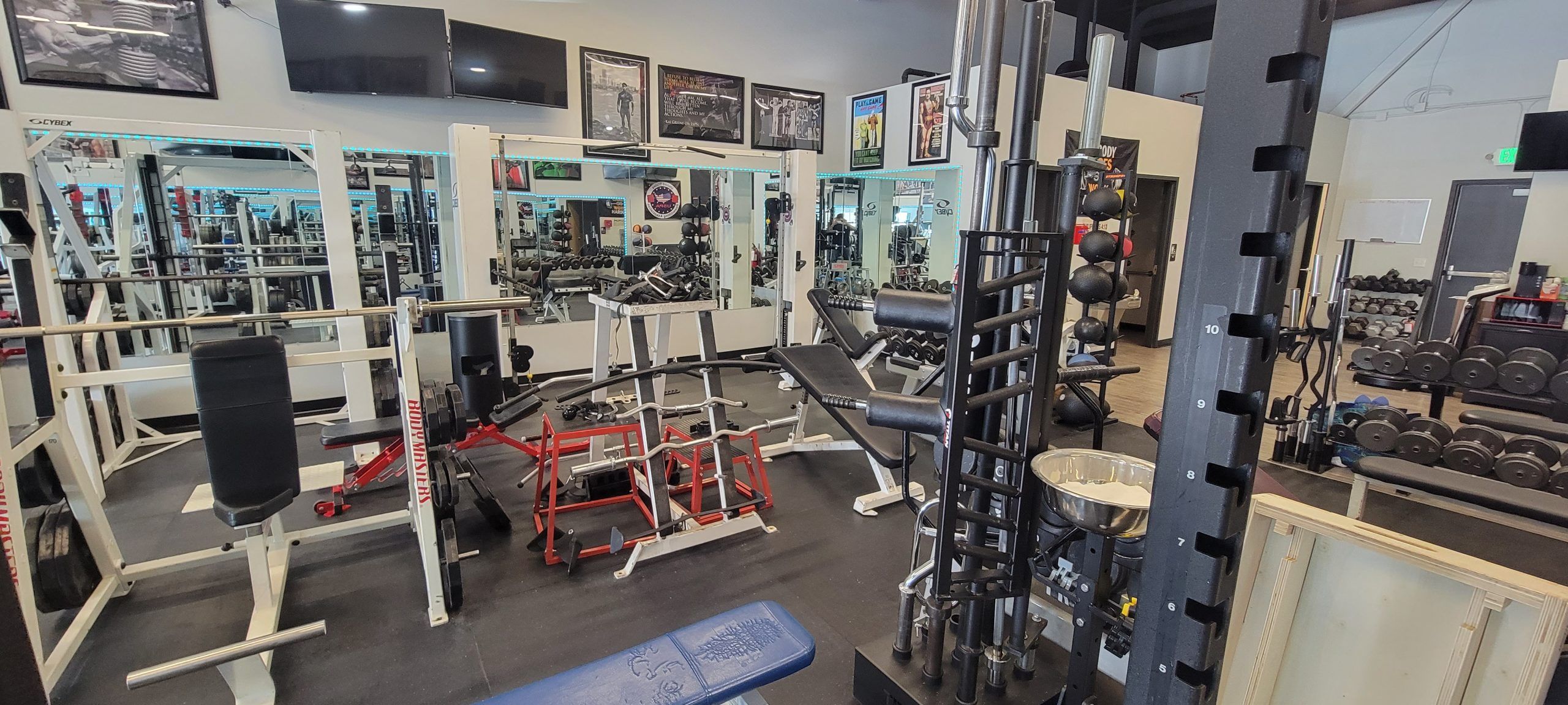 Squat rack with a chalk bowl next to a red lever machine, benches and a dumbbell rack